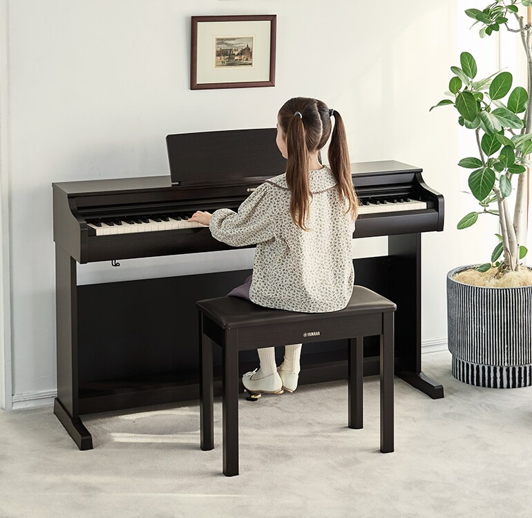 A young girl practicing on an ARIUS piano in a living room