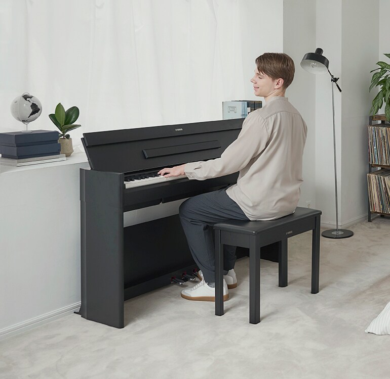 A man playing an ARIUS piano in a bedroom in a relaxed setting